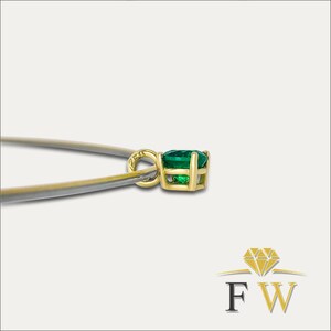 May include: A gold pendant with a vibrant green gemstone. The pendant is held by tweezers, showcasing the intricate setting and the gem's brilliance. The pendant is a classic jewelry piece.
