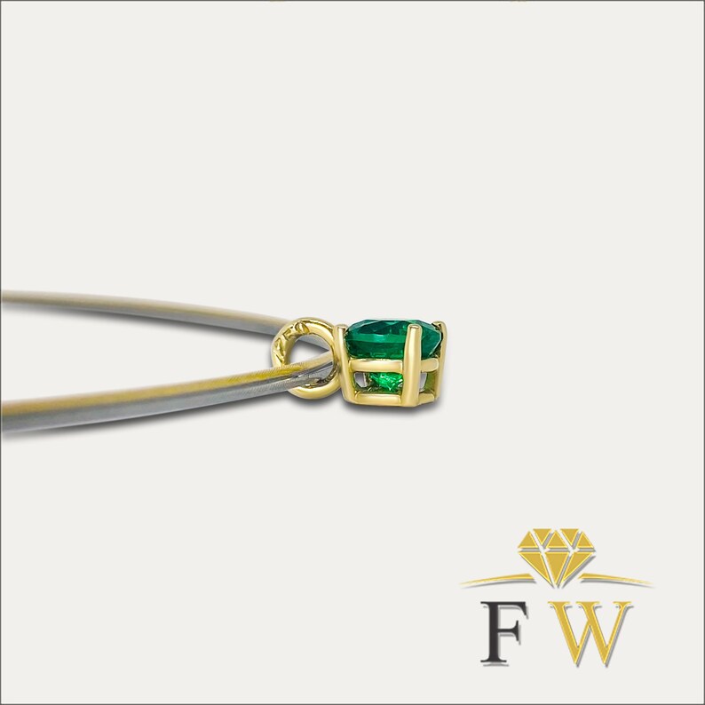 May include: A gold pendant with a vibrant green gemstone. The pendant is held by tweezers, showcasing the intricate setting and the gem's brilliance. The pendant is a classic jewelry piece.