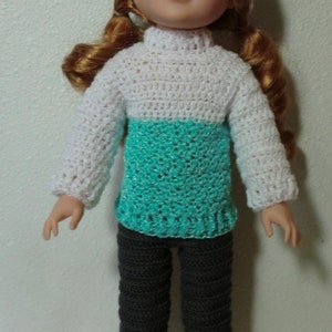 May include: A doll wearing a white and turquoise crocheted sweater, gray crocheted pants, and a white crocheted hat with a turquoise band.