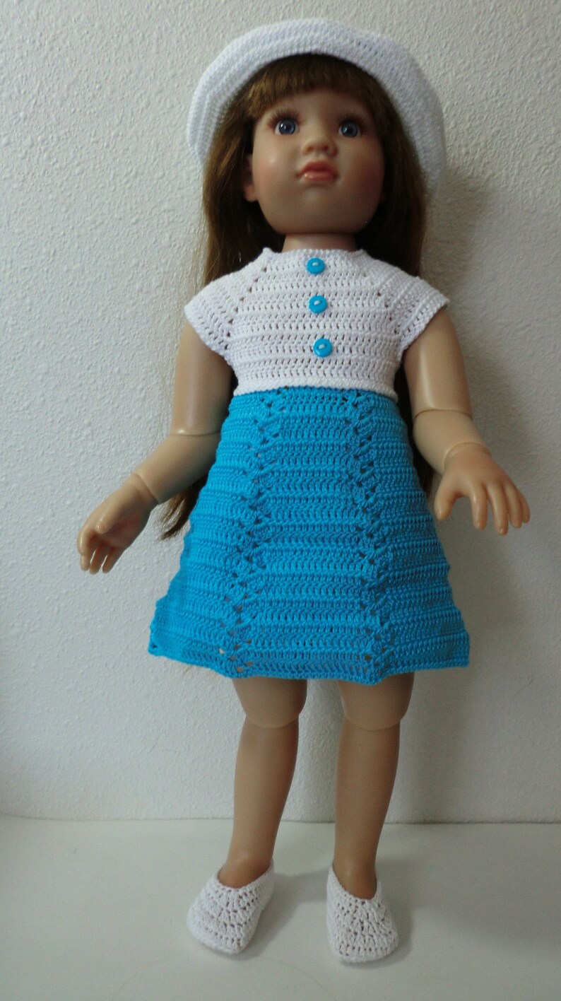 May include: A doll wearing a white crocheted hat, a white crocheted top with blue buttons, and a blue crocheted skirt. The doll is wearing white crocheted shoes.
