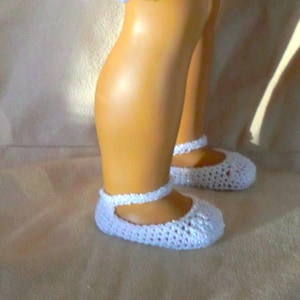 May include: A pair of white crocheted doll shoes with a strap across the top.