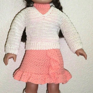 Peut inclure: Une poupée portant un pull en crochet blanc avec un col roulé couleur pêche, une jupe en crochet pêche avec un volant et des chaussettes en crochet blanc.