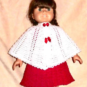 May include: A white crocheted doll cape with red bows, worn by a doll with brown hair and a red skirt.
