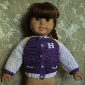 Puede incluir: Una chaqueta de punto de color morado y blanco con ribete amarillo y una letra 'H' blanca en la parte delantera. La chaqueta la lleva una muñeca con el pelo castaño.