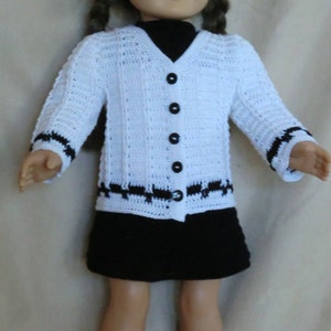 May include: A white crocheted cardigan with black trim and black buttons. The cardigan is worn by a doll with brown hair and blue eyes. The doll is wearing a black skirt.