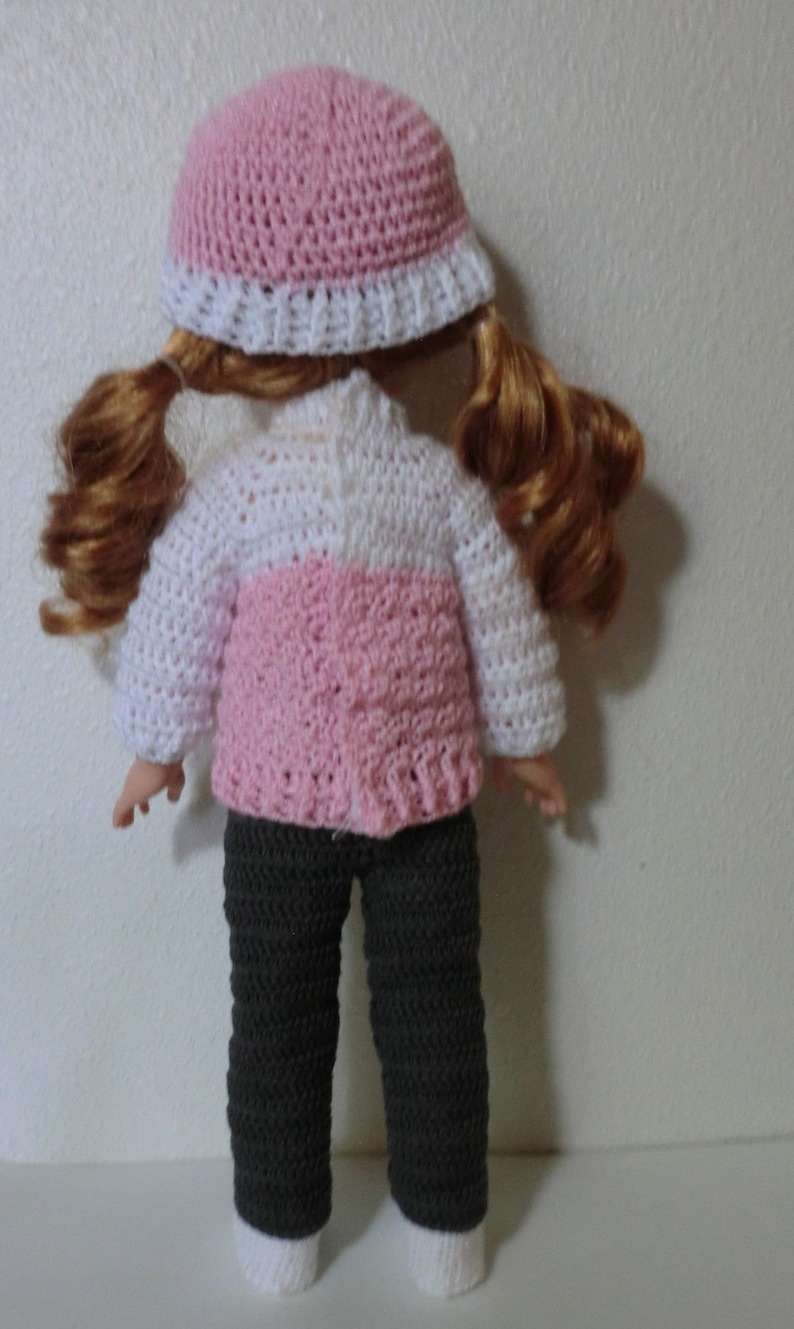 May include: A doll wearing a pink and white crocheted sweater, a pink crocheted hat, and gray crocheted pants.