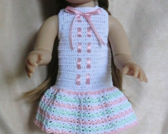 May include: A doll wearing a white crocheted dress with pink and green stripes, a white crocheted hat, and brown hair.