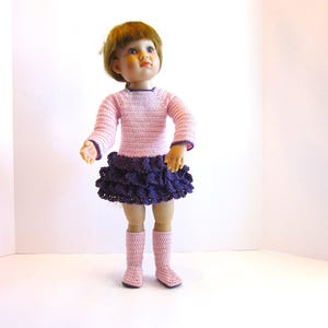 May include: A doll wearing a pink and purple crocheted dress and pink boots. The doll has blonde hair and blue eyes.