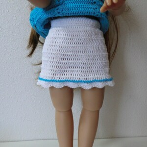May include: A white crocheted skirt with a blue crocheted trim. The skirt is worn by a doll.