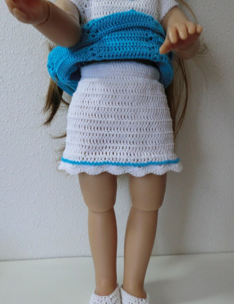 May include: A white crocheted skirt with a blue crocheted trim. The skirt is worn by a doll.
