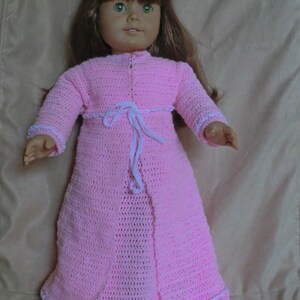 May include: A pink crocheted doll dress with white trim and a white tie at the waist.