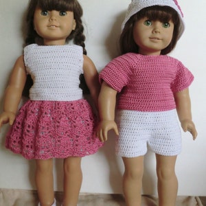 May include: Two dolls wearing crocheted outfits. The doll on the left is wearing a white crocheted top and a pink crocheted skirt. The doll on the right is wearing a pink crocheted top and white crocheted shorts. Both dolls have brown hair and are wearing white shoes.