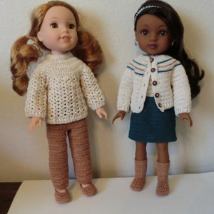 May include: Two dolls wearing crocheted outfits. The doll on the left is wearing a cream sweater and brown pants. The doll on the right is wearing a cream cardigan with a teal skirt and brown socks.