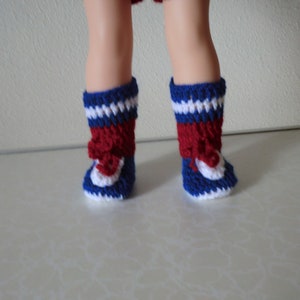 May include: A pair of red, white, and blue crocheted doll boots. The boots have a white toe and heel, a red middle section, and a blue top.