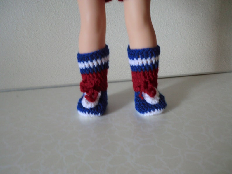 May include: A pair of red, white, and blue crocheted doll boots. The boots have a white toe and heel, a red middle section, and a blue top.