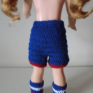 May include: Blue and red crocheted shorts with a white stripe on the legs. The shorts are made for a doll.