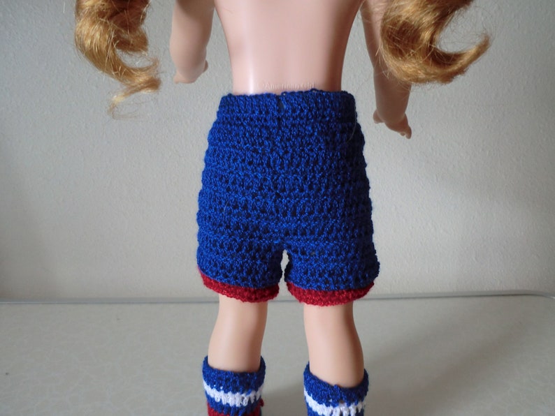May include: Blue and red crocheted shorts with a white stripe on the legs. The shorts are made for a doll.