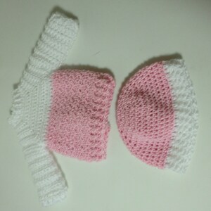 May include: A pink and white crocheted hat and matching long-sleeved top.
