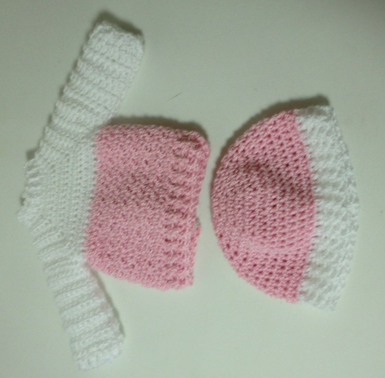 May include: A pink and white crocheted hat and matching long-sleeved top.