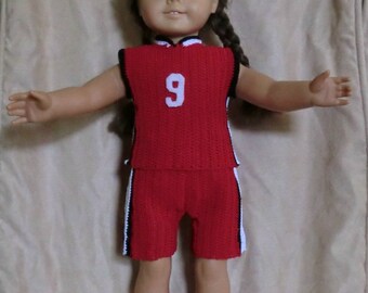 Puede incluir: Una muñeca con un uniforme de baloncesto de crochet rojo y blanco con el número 9 en la parte delantera. La muñeca lleva zapatillas blancas con cordones negros.