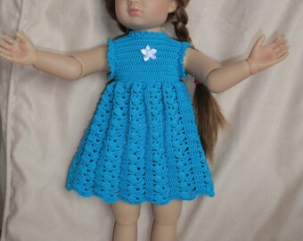 May include: A doll wearing a blue crocheted dress with a white flower accent. The dress has a scalloped hem and is sleeveless.