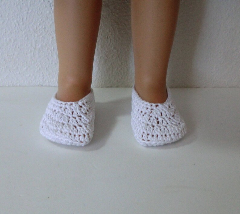May include: White crocheted doll shoes. The shoes are made with a delicate, open-stitch pattern.