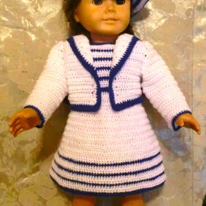 Puede incluir: Un vestido de marinero de crochet blanco con rayas azules y un sombrero de marinero de crochet blanco a juego. El vestido tiene un cuello de marinero y una chaqueta de crochet con ribetes azules.