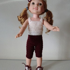 May include: A doll wearing a white crocheted tank top, maroon crocheted pants, and maroon shoes with white accents. The doll has red hair in pigtails and is wearing a white and maroon headband.