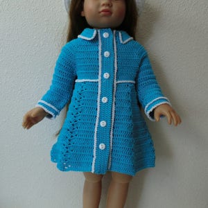 May include: A blue crocheted dress with white trim and buttons, worn by a doll with brown hair and a white crocheted hat. The doll is wearing white crocheted shoes.