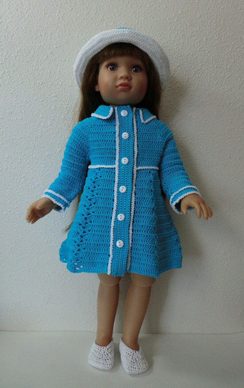 May include: A blue crocheted dress with white trim and buttons, worn by a doll with brown hair and a white crocheted hat. The doll is wearing white crocheted shoes.