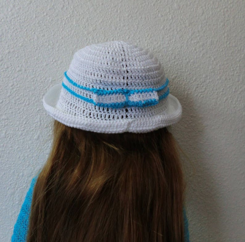 May include: White crocheted sun hat with a blue ribbon trim. The hat has a wide brim and is made with a delicate crochet stitch.