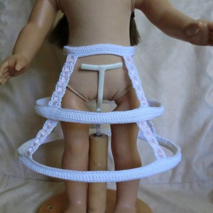 May include: A white doll crinoline with pink ribbon trim. The crinoline has three tiers and is made of a crocheted material.
