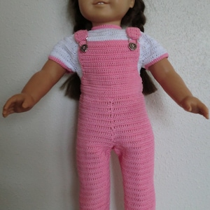 Puede incluir: Un conjunto de mono de crochet rosa con ribetes blancos y botones plateados, usado por una muñeca con cabello castaño.