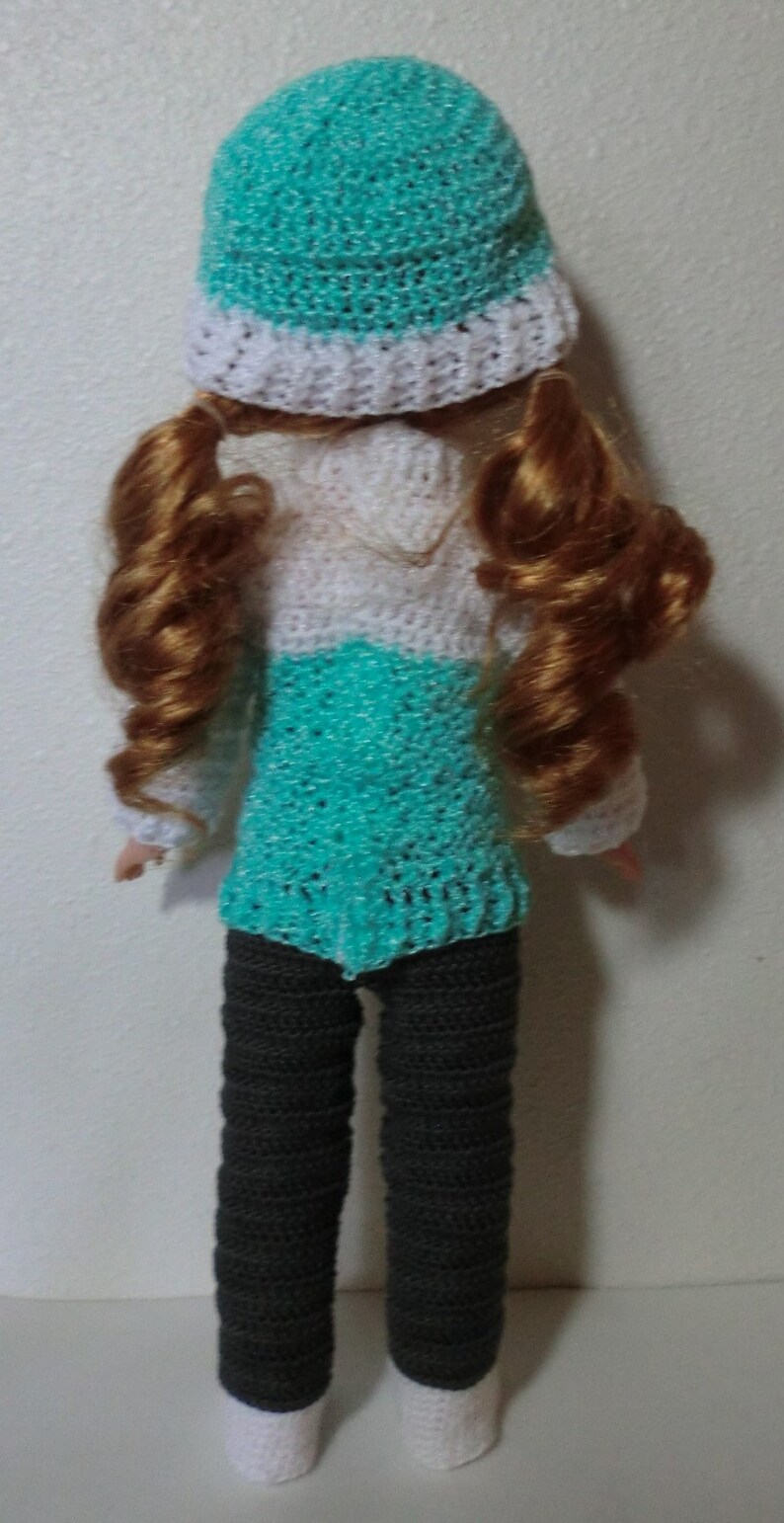 May include: A crocheted doll wearing a teal and white hat, a teal and white sweater, and gray pants with white cuffs.