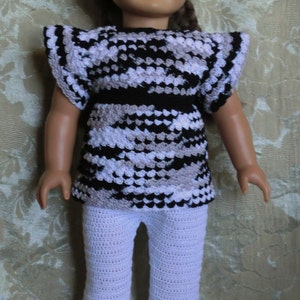 May include: A doll wearing a black and white crocheted top with a white crocheted skirt. The doll has brown hair and blue eyes.
