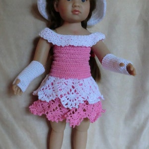 May include: A doll wearing a pink and white crocheted dress with a white crocheted hat and matching wristlets. The doll has brown hair and blue eyes.