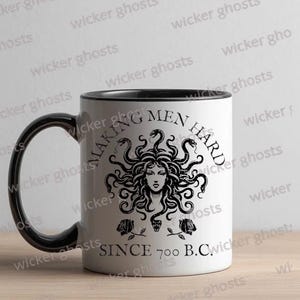 May include: White ceramic mug with a black interior, handle, and rim. The mug features a black illustration of Medusa with the text "MAKING MEN HARD SINCE 700 B.C." in a circular design. The mug has a glossy finish.