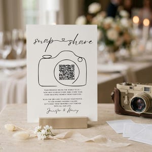 May include: A white rectangular wedding sign featuring the black text snap share, a line-art camera illustration with a central QR code, and the names Jennifer & Henry. The sign includes instructions to scan the code to upload photos.