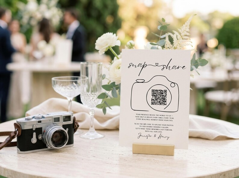 May include: A white rectangular wedding sign with black text and a line-art camera illustration containing a QR code. The sign reads snap share, includes instructions to upload photos to a shared gallery, and is signed by Jennifer and Henry.