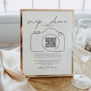 Puede incluir: Un letrero enmarcado con borde dorado presenta las palabras "snap share" sobre una ilustración de cámara y un código QR. El texto de abajo dice: "Tu presencia significa el mundo para nosotros..." e invita a los invitados a subir fotos.