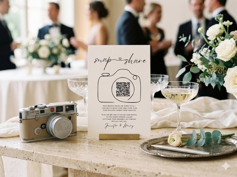 May include: A rectangular white wedding sign featuring the text "snap & share" above a line-art camera icon containing a QR code. Below the icon, the text reads "Your presence means the world to us - now help us relive every smile, every tear, every beautiful moment from your eyes. Scan the QR code to upload your photos to our shared wedding gallery. Let's make these memories last forever. With all our love, Jennifer & Henry."