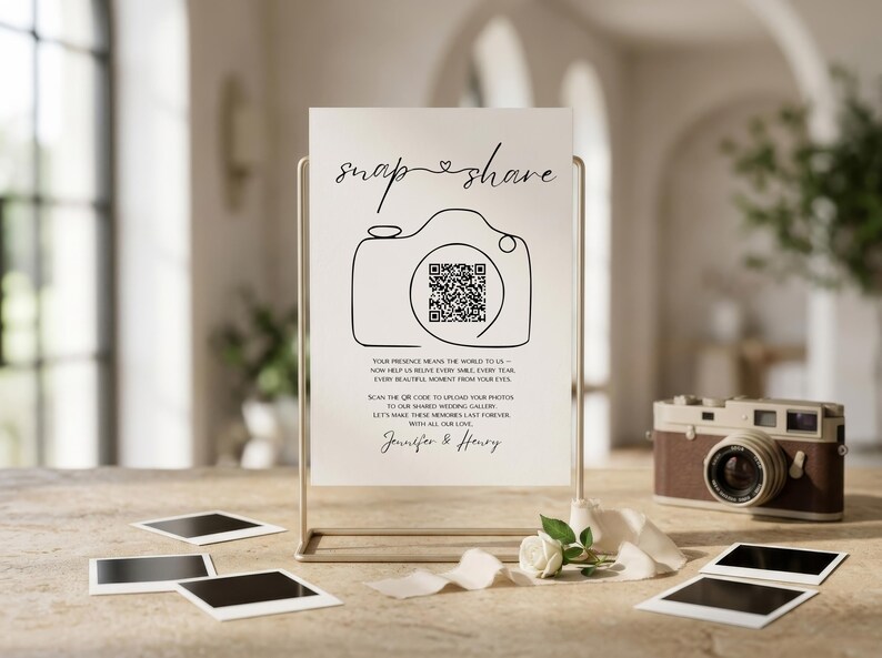 May include: A white rectangular sign in a gold metal stand featuring the text snap share, a line-art camera icon with a QR code in the center, and the names Jennifer & Henry. The sign includes instructions for guests to upload photos.