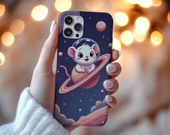 Peut inclure: Coque de téléphone avec une souris de dessin animé portant un casque spatial, chevauchant une planète avec des anneaux, sur fond bleu foncé étoilé. Le boîtier a une bordure violette et une découpe pour l'appareil photo.