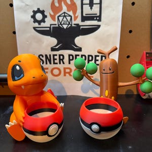 May include: Orange Charmander figure and two red, white, and black Poke Ball planters. A brown wooden figure with green spheres is also visible. The background features a sign with a logo and the text "SNER PEPPER FOR".