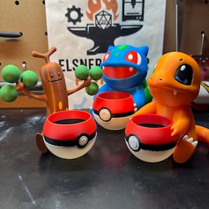 May include: A collection of 3D-printed Pokémon-themed planters. The planters are designed as Pokéballs, with a red top, white bottom, and black stripe. The figures include a brown Sudowoodo, a blue Bulbasaur, and an orange Charmander.
