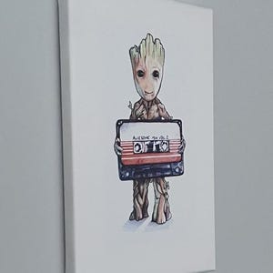 以下が含まれることがあります： レトロなカセットテープを持った、木のような漫画のキャラクターが描かれたキャンバスプリント。テープには「AWESOME MIX VOL. 2」と書かれています。キャラクターは茶色とベージュで、テープには赤と白のストライプが入っています。