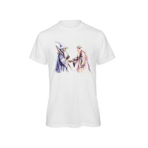 Peut inclure: T-shirt blanc avec une illustration à l'aquarelle de deux sorciers, l'un en bleu et l'autre en beige, se tenant la main. Les sorciers sont représentés avec de longues barbes et des robes, sur fond blanc. Le motif est centré sur le t-shirt.