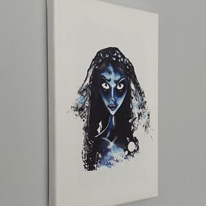 May include: A canvas print featuring a stylized illustration of a blue-skinned woman with dark hair and large eyes. The artwork has a watercolor effect, with splashes of blue and white. The canvas is mounted on a wooden frame.