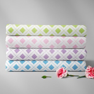 Pode incluir: Quatro peças de tecido enroladas com padrões de losangos em verde, rosa, roxo e azul. Cada rolo é empilhado um em cima do outro. Dois cravos cor-de-rosa com caules e folhas verdes estão em primeiro plano.