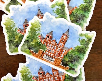 May include: A watercolor illustration of a brick building with two towers, surrounded by green trees. The building has a sign that reads "Auburn University".
